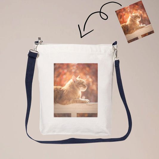 A beige canvas crossbody bag with one or two sided print with photos. The bag has a long strap that can be worn over the shoulder or across the body.